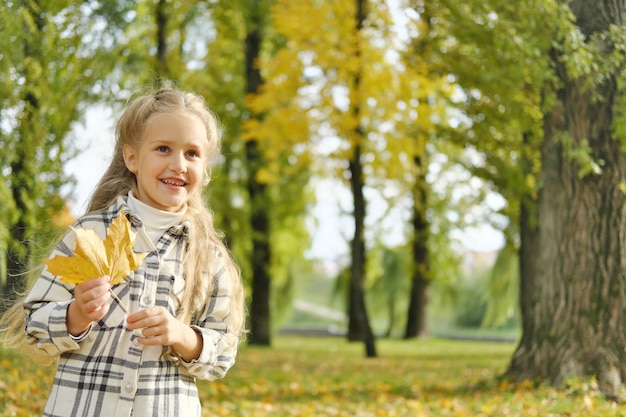 A little blonde girl holds an autumn leaf in her hands and looks away Horizontal photo