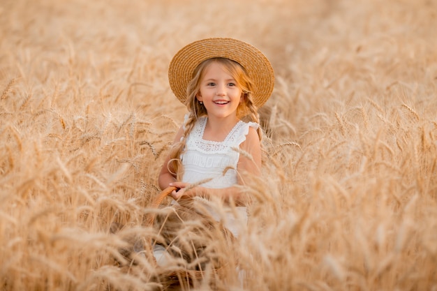 little blonde girl holds a basket of bread in a wheat field