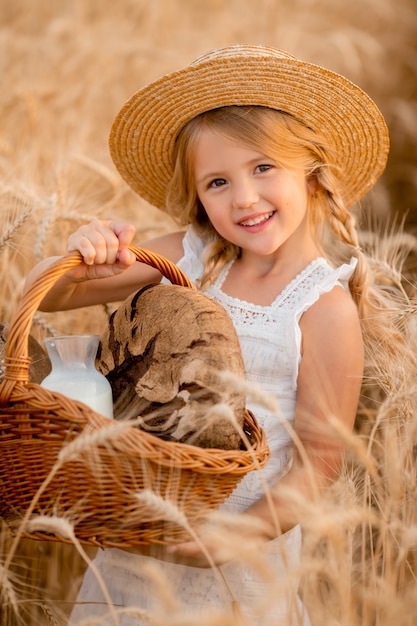A little blonde girl holds a basket of bread in a wheat field