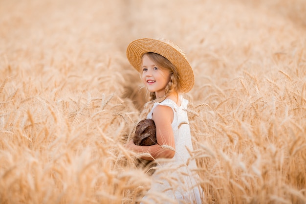 little blonde girl holds a fresh loaf of bread in a wheat field in the summer