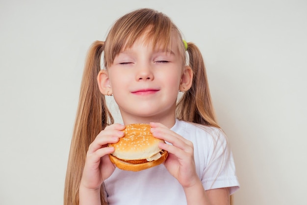 小さなブロンドの女の子は野菜と一緒に焼き菜食主義のハンバーガーを食べています子供ビーガンのアイデア健康的な食事の概念