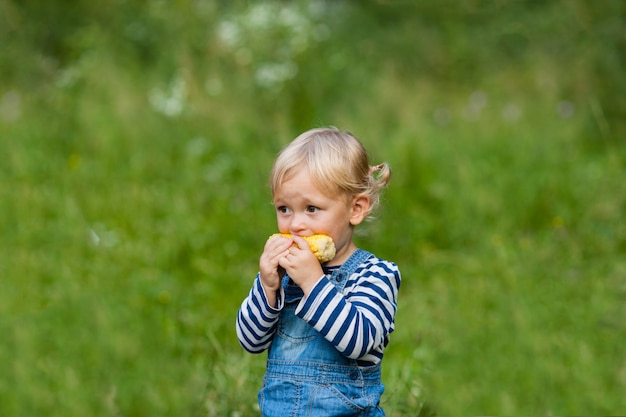 La piccola ragazza bionda sta mangiando mais al campeggio