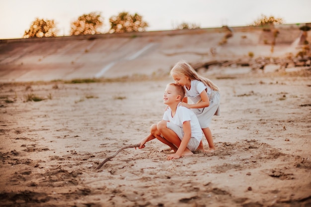 Photo a little blonde girl kisses the top of a boy's head on a sandy beach. sunset. copy space