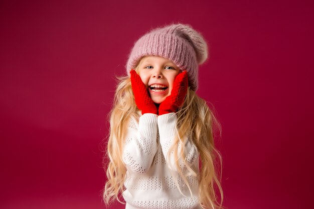 little blonde girl in a knitted hat and mittens smiles. winter clothes