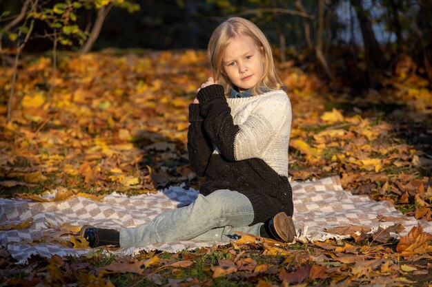 La piccola ragazza bionda si trova su una coperta nel parco in autunno