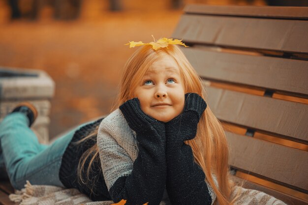 Little blonde girl lies on a park bench with a leaf on her head