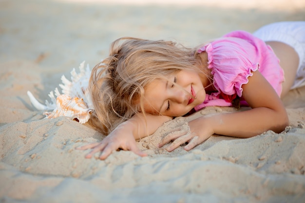 little blonde girl lying on a sandy beach smiling