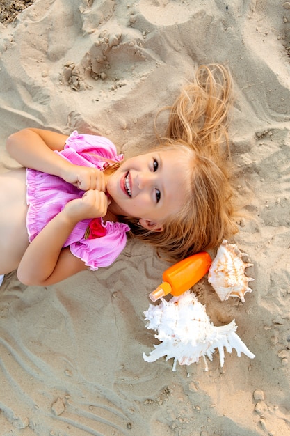 little blonde girl lying on a sandy beach smiling