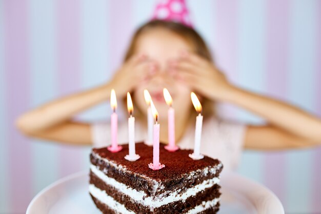 La piccola ragazza bionda in protezione rosa di compleanno che sorride vicino i suoi occhi esprime un desiderio