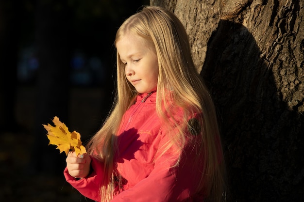 Little blonde girl in a pink jacket in the park in autumn