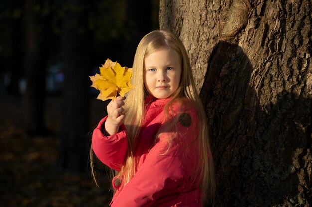 Little blonde girl in a pink jacket in the park in autumn