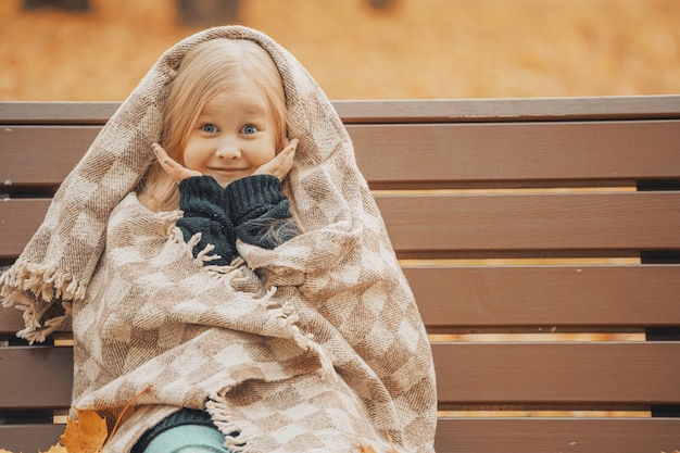 Little blonde girl in a plaid in the park on a bench