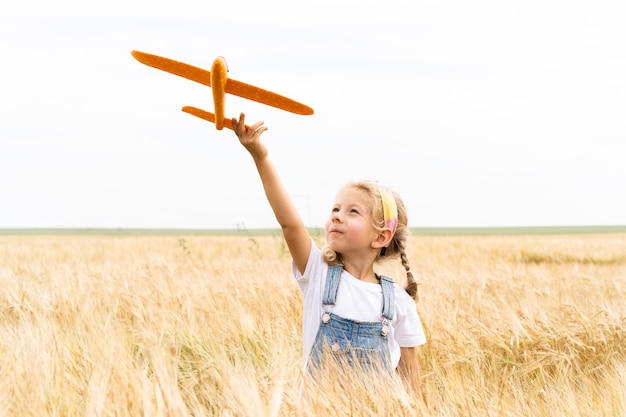 Little blonde girl plays plane in the field of rye, grain harvest.