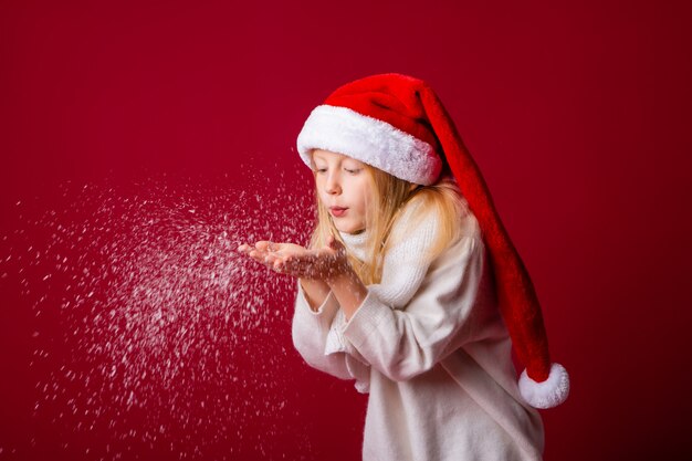 Little blonde girl in a Santa suit blows snow off her hands