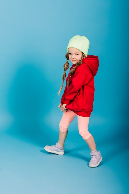 Bambina bionda, lei ride, seduta sul pavimento, in posa isolata sull'azzurro. infanzia, moda.