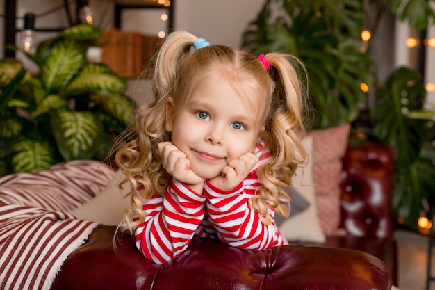 Little blonde girl sits on the couch at home and laughs. stay at home