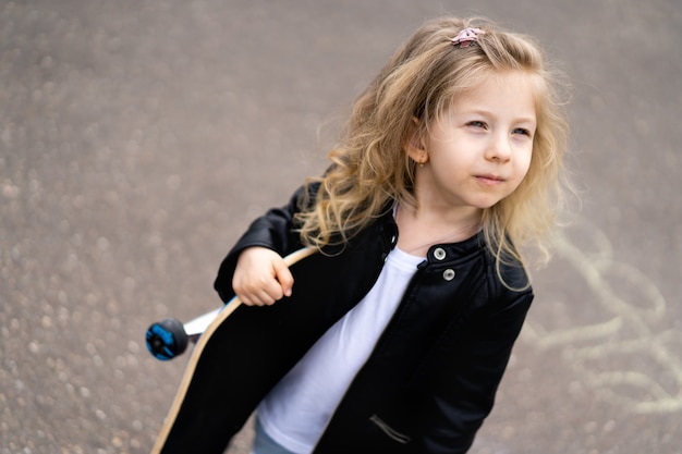 Little blonde girl on a skateboard in the city.