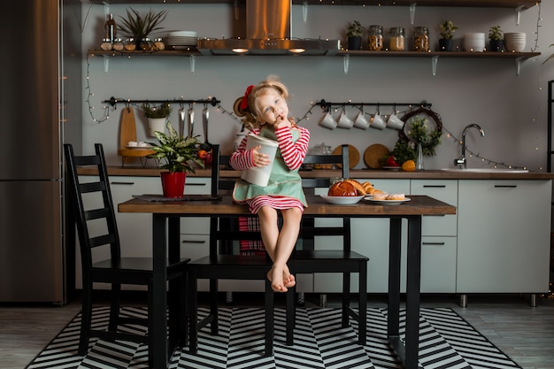 Little blonde girl smiles in the kitchen, cooks a cake. Child in the kitchen. Stay at home