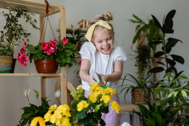 little blonde girl sprays from a bullet dispenser or waters indoor flowers caring houseplants