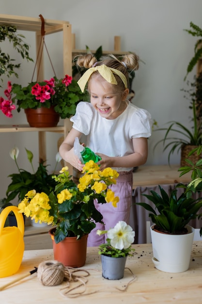 маленькая блондинка брызгает из пульверизатора или поливает комнатные цветы Домашнее садоводство