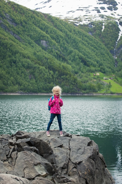 Little blonde girl standing at the shore of norwegian lake