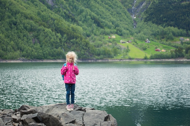 Little blonde girl standing at the shore of norwegian lake