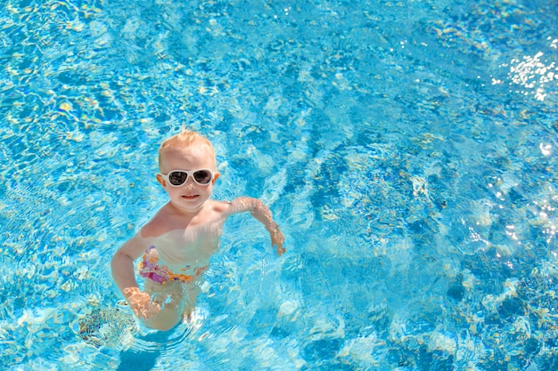 Little blonde girl swims in the pool with blue water