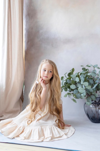 Photo little blonde girl in vintage dress near retro background and vase with green branches eucalyptus gum tree happy childhood simple and cozy life happy easter eggs hunt