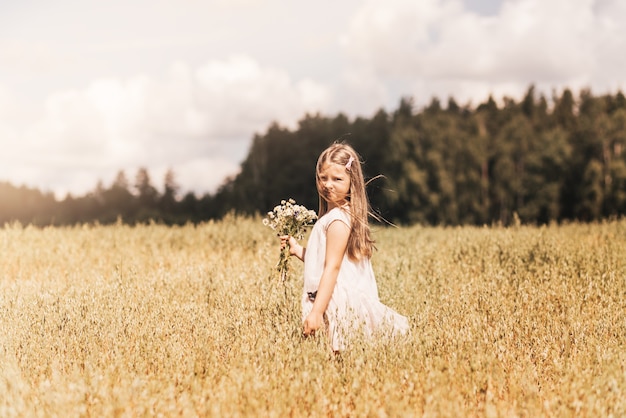 A little blonde girl walks through a golden field in the summer. Concept of purity, growth, happiness