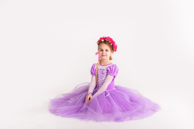 Маленькая белокурая девушка нося фиолетовое fairy платье принцессы на белой предпосылке. Детский костюм для новогодней вечеринки