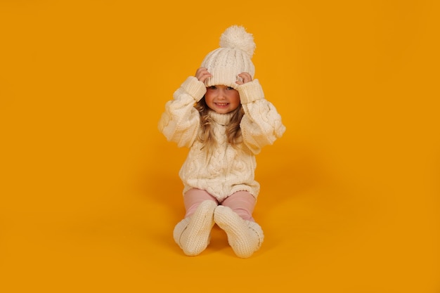 a little blonde girl in a white knitted sweater a white hat and knitted socks