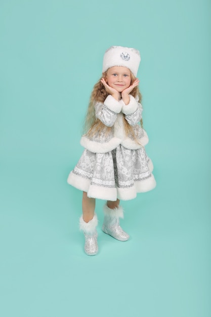 a little blonde girl with blue eyes in a New Years snow maiden costume on a blue background