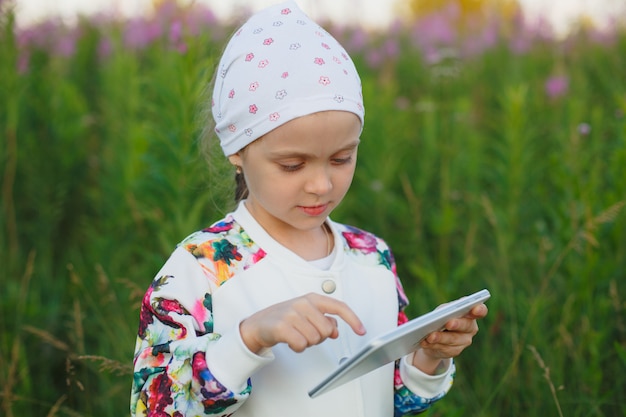 Little blonde girl with digital tablet on the nature