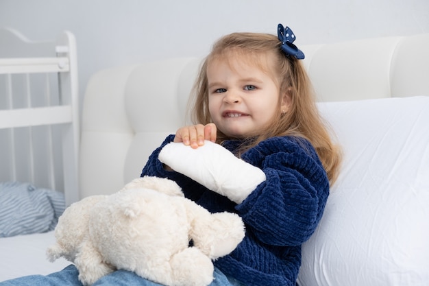 Little blonde girl with hand in cast sitting in bed.