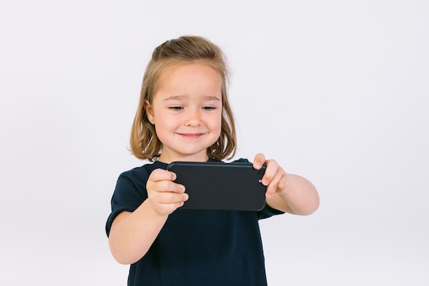 Little blonde girl with mobile phone in her hands, playing a game