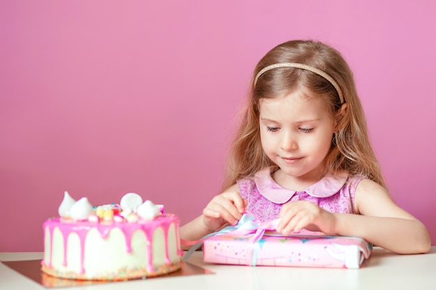 A little blonde girl with a pink cake with candles