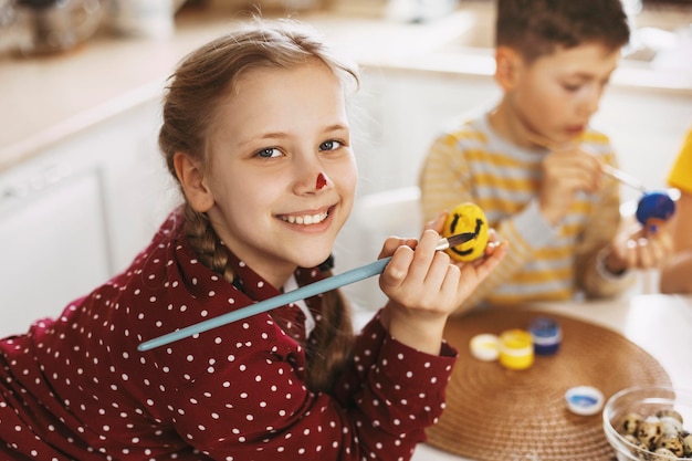 Photo little blonde at home in the kitchen paints easter eggs in different colors for easter