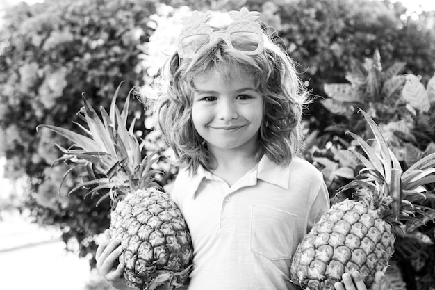 Little blonde kid hugging pineapple on nature background Childhood healthy nutrition advertising Close up kids funny face copy space