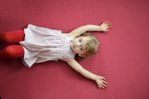 Little blonde lying on a dark pink background.