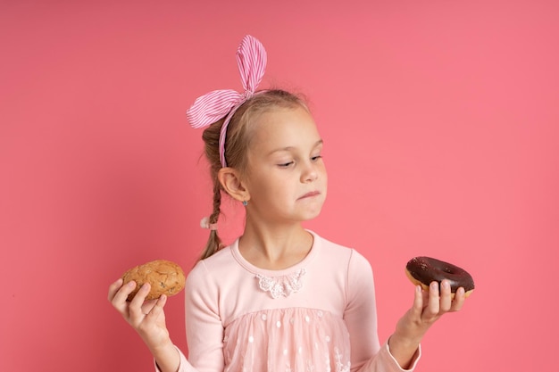 Little blonde model in dress with headband and pigtail holding bun and chocolate donut 