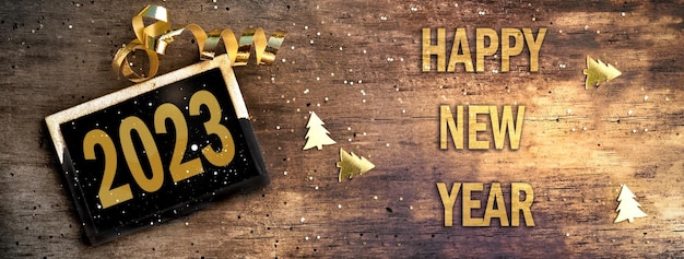 Little board on rustic wooden background with golden confetti and ribbon new year 2023