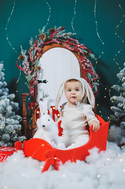 クリスマスツリーの背景にうさぎのスーツを着た1歳の男の子 ⁇ 小さな子供のためのクリスマス衣装 ⁇ 新年