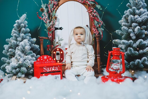 A little boy 1 year old in a bunny suit is sitting near the Christmas tree New Year's mood bunny costume for children