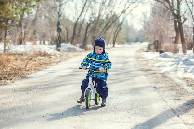 A little boy 2 years old learns to ride a balance bike on the road in the village