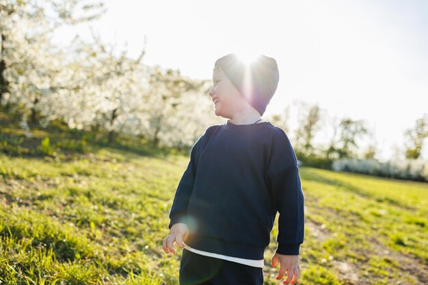 A little boy 3 years old in a sweater and a hat runs through a blooming garden clothes for children aged 3 years a happy eotian child is white among blossoming apple trees