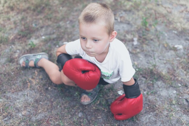 A little boy 45 years old wearing red boxing gloves on the street