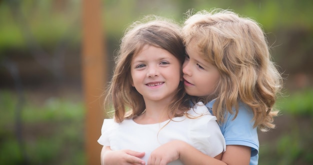 写真 小さな男の子と女の子の親友が夏の公園で愛を込めてお互いにキスしている子供たちを抱き締める幸せな子供たち