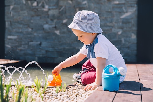 Little boy in beautiful zen garden with watering can near fountain Child playing outdoors in spring or summer Family on nature in Arboretum Slovenia