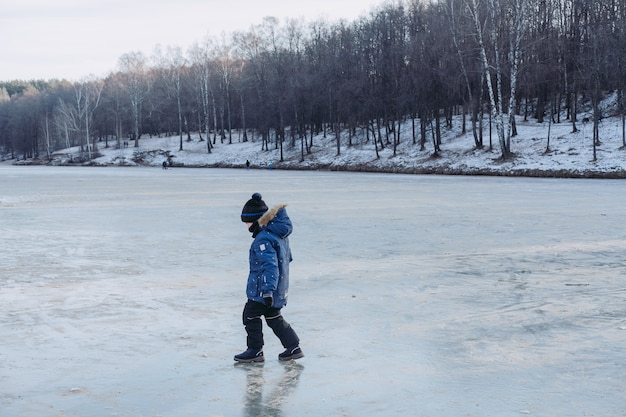 Little boy on big frozen lake near the forest.