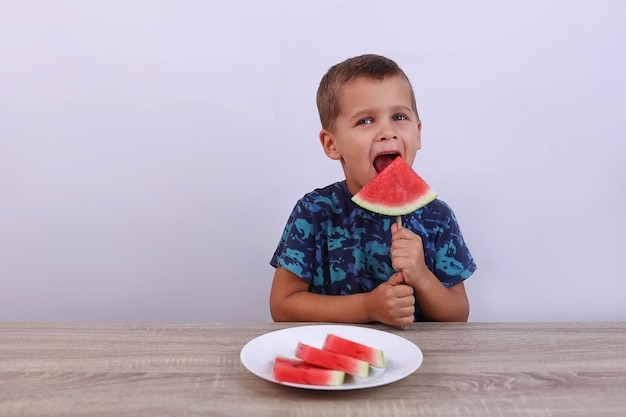 little boy bites off a watermelon on a stick